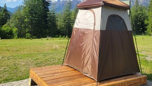 A tent set up on a wooden platform in a grassy field with a mountain backdrop.