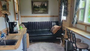 A compact kitchen with a wooden countertop, a black leather sofa, and a dining area with two bar stools.