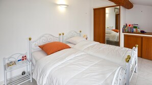 A double bed with white bedding and an orange pillow, a bedside table with a book and a red object, and a wooden door leading to a bathroom. - Beautiful home in Aubignan (Aubignan)