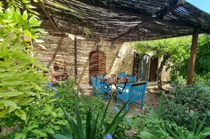 Relax in a tranquil outdoor space with a stone wall, thatched roof, and lush greenery.