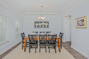 Uma sala de jantar com mesa e cadeiras de madeira, um candelabro e uma obra de arte emoldurada na parede.