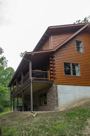 A two-story log cabin with a balcony and a stone foundation. - Night Song Lodge | Hocking Hills, New, Sleeps 16 (Logan)