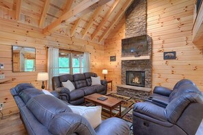 A cozy log cabin interior with a stone fireplace, leather sofas, and a large mirror.