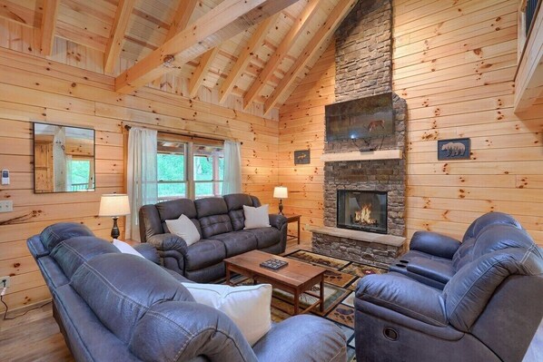A cozy log cabin interior with a stone fireplace, leather sofas, and a large mirror.