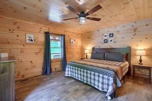 A wooden-paneled bedroom with a bed, two bedside tables, a ceiling fan, and wall-mounted pictures.