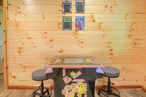 A small wooden table with a black surface and two stools. Above the table, there are four arcade game tokens displayed on the wall.