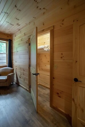 Een houten interieur met een deur die leidt naar een kamer met een bed en een raam.