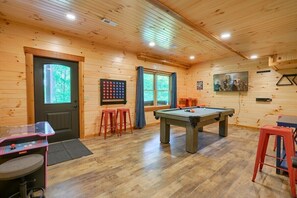 A wooden interior with a pool table, a dartboard, and a ping pong table.