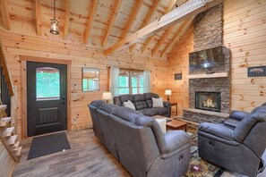 A log cabin interior with a fireplace, leather sofas, and a wooden ceiling.