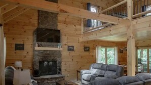 Ein Blockhaus-Interieur mit Kamin aus Stein, einer Couch, einem Tisch und einem Deckenventilator.