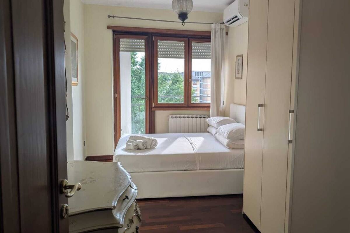 A bedroom with a bed, a radiator, and a window with blinds.