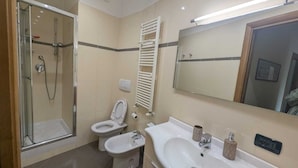 Et badeværelse med bruseniche i glas, toilet, bidet og et spejl over vasken.