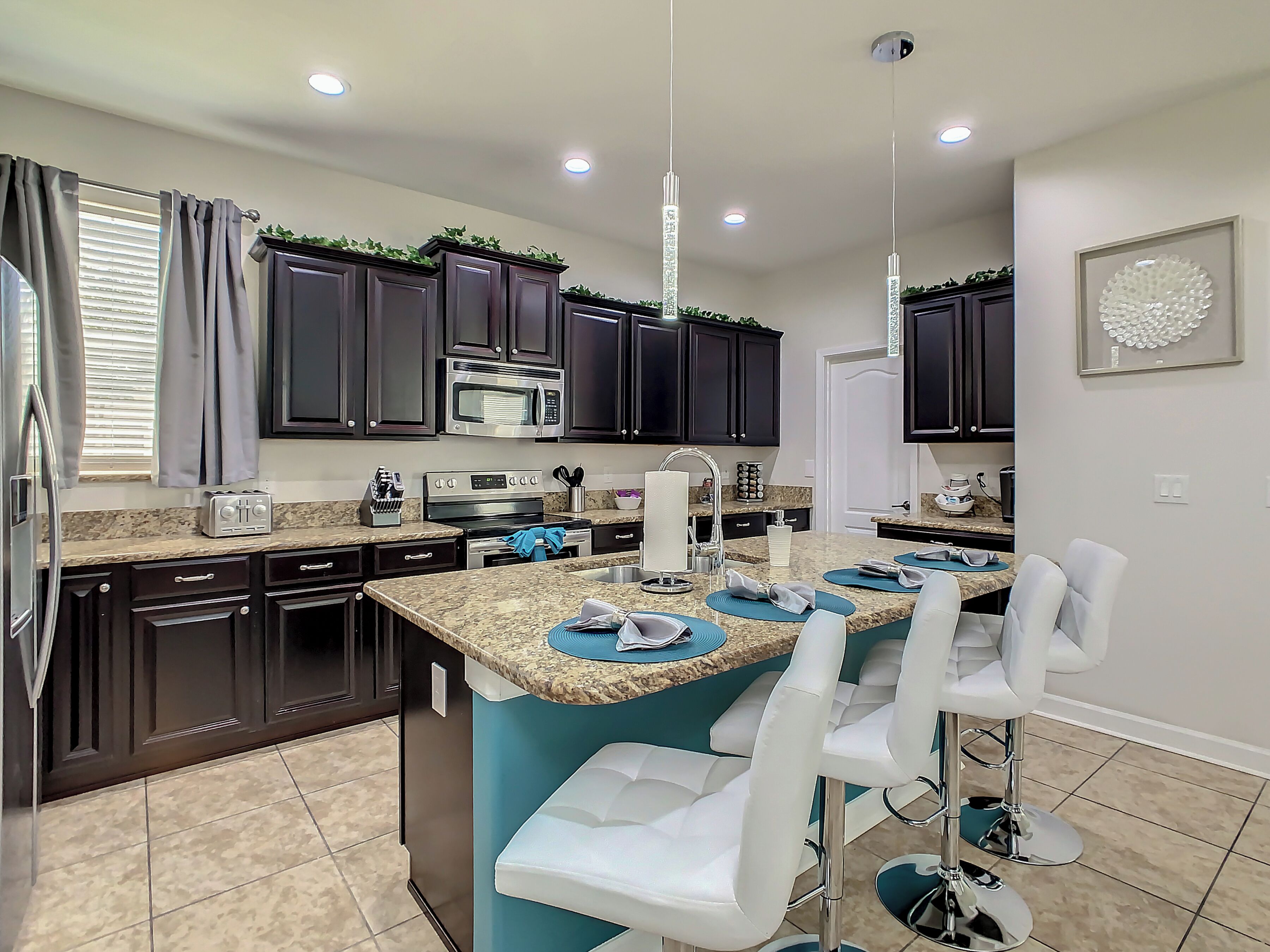 A modern kitchen with dark cabinetry, a granite countertop, a built-in microwave, and a stainless steel oven. There are bar stools and a small island with a blue countertop.