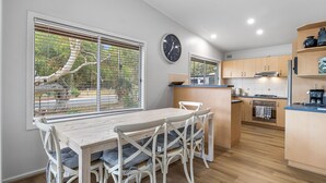 Een moderne keuken met houten kastjes, een centraal eiland en een eethoek met witte stoelen en gestreepte kussens.