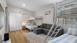 Een kleine kamer met stapelbedden, een slaapbank, een bureau en een kledingkast.