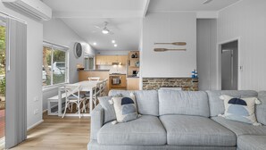 Een moderne woonkamer met een grijze bank, een eethoek met een witte tafel en stoelen, een keuken met houten kasten en een stenen open haard.