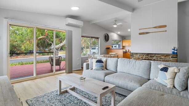 Een moderne woonkamer met een grijze bank, een houten salontafel en uitzicht op een boom door grote schuifdeuren van glas.