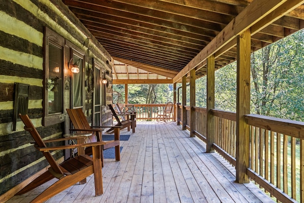 A wooden deck with chairs and a table, surrounded by a wooden railing, overlooking a forested area.
