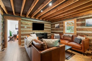 A log cabin interior with a leather sofa, a flat-screen TV, and wooden beams.