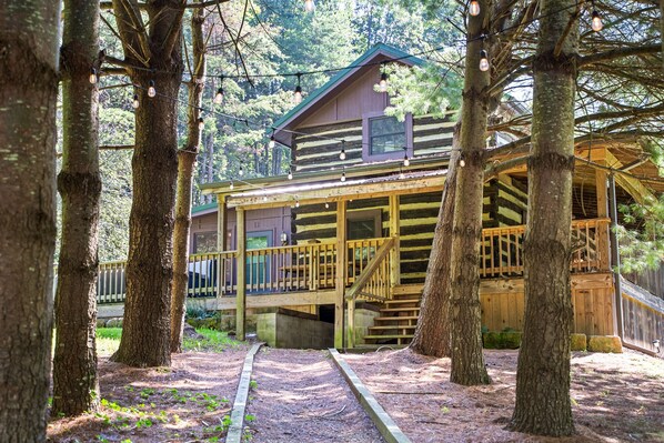 A cabin with a wooden deck and a covered porch, surrounded by trees.