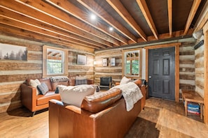 A log cabin interior with a wooden ceiling, a leather sofa, a small table, and a door.