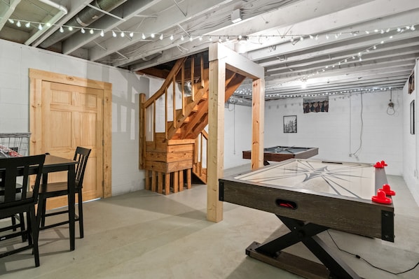 Ein Zimmer mit einer Holztreppe, einem Esstisch mit Stühlen und einem Billardtisch.