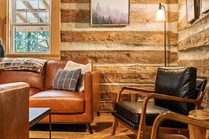 A cozy log cabin interior with a leather sofa, a wooden chair, and a small table.