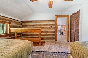 Ein Schlafzimmer in einer Blockhütte mit Etagenbett, Deckenventilator aus Holz und Blick auf eine Holztreppe, die in einen anderen Raum führt.