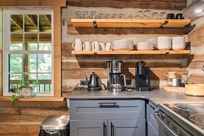 A kitchen with wooden shelves holding cups and plates, a coffee maker, and a kettle.
