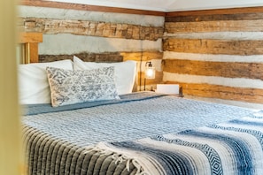 Ein Bett mit gesteppter Bettdecke, einem Holz-Kopfteil und einer Wand mit freiliegenden Ziegelsteinen und Holzbalken.