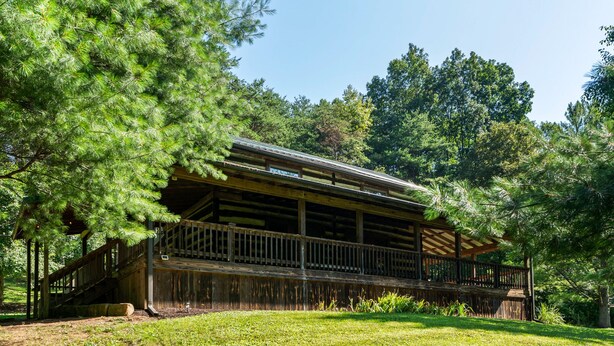 A wooden cabin with a balcony, surrounded by trees and grass.