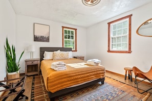 A bedroom with a bed, nightstands, a chair, a desk, a potted plant, and a window.