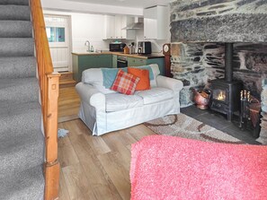 Una sala de estar con sofá, chimenea, una cocina al fondo y una escalera.
