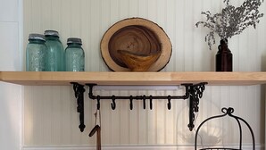 A kitchen counter with a wooden shelf holding jars, a wooden bowl, and a vase with flowers.
