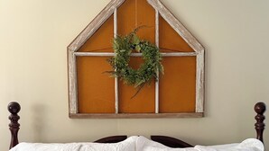 A bedroom with a bed, two pillows, a wooden headboard, and a wall-mounted decoration.