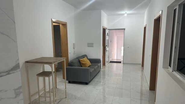 Un pasillo amplio con comedor, un sofá y una puerta que da a otra habitación.