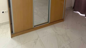 Una habitación con un armario corredero de madera con puerta de espejo, suelo de baldosas y una cortina a la derecha.