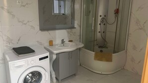 Un baño con lavadora, lavamanos y ducha con mampara de vidrio.