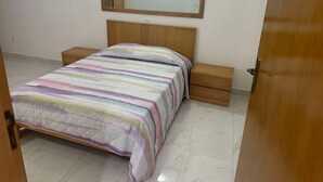Un dormitorio con cama, mesita de noche, cajón, cabecera de madera y un espejo en la pared.