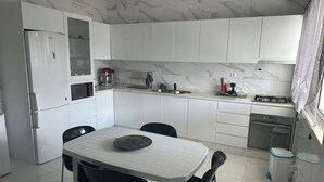 Una cocina moderna con gabinetes blancos, una mesa de comedor con sillas, horno empotrado y estufa a gas.