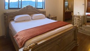 Ein großes Bett mit hölzernem Kopfteil, einer roten Tagesdecke und zwei Kissen.