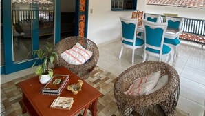 Ein Zimmer mit Korbmöbeln, einem Holztisch und einem blau-weißen Stuhlgarnitur.