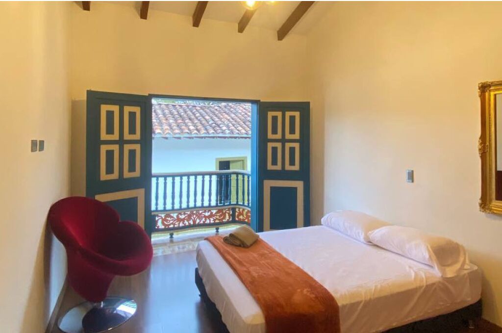 A bedroom with a bed, a red chair, and an open door leading to a balcony.