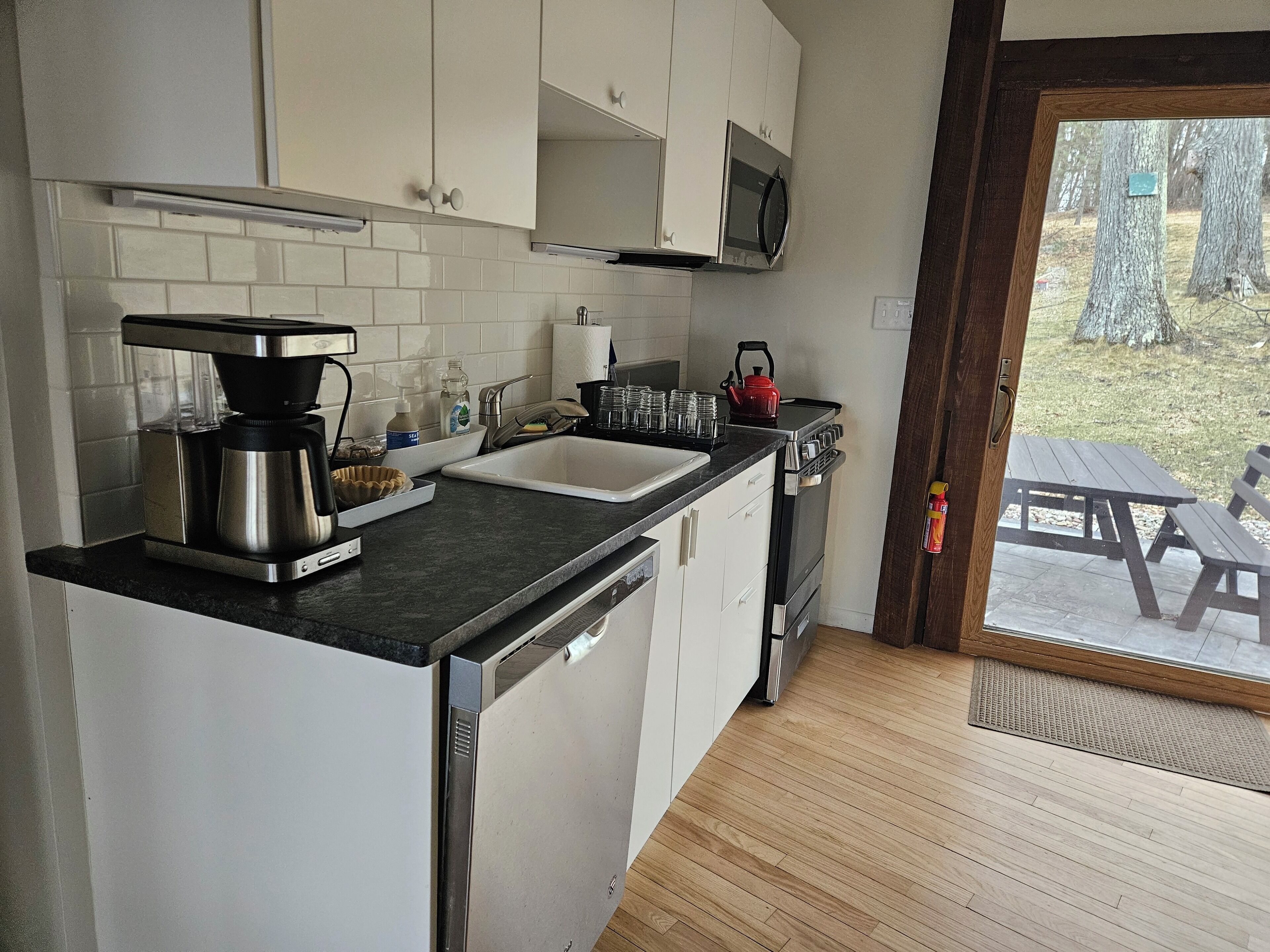Una cocina moderna con armarios blancos, una cafetera de acero inoxidable, un hervidor y un lavamanos.