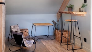 A cozy attic room with a sloped ceiling, a rocking chair, a small wooden table, and a high bar stool. - La Cabane - deux chambres et grande terrasse  ⭐️⭐️⭐️ (Metz)
