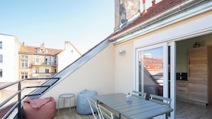 A balcony with a table and chairs, a bean bag, and a sliding glass door leading to a kitchen area. - La Cabane - deux chambres et grande terrasse  ⭐️⭐️⭐️ (Metz)