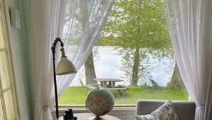 A cozy room with two grey armchairs, a small round table with a globe, and a view of a lake through sheer curtains.