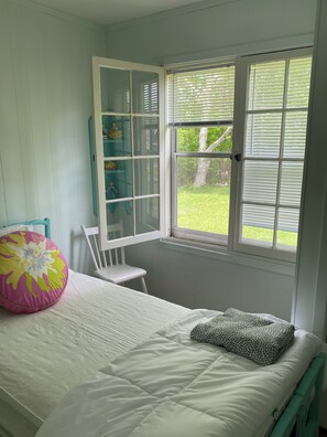 Cozy retreat with a single bed, teal chair, and a window with white blinds.