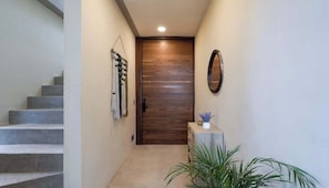 Un couloir avec une porte en bois, un escalier et une plante.