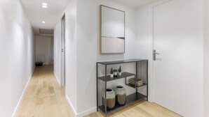 Ein Flur mit Holzboden, einer weißen Tür, einem gerahmten Kunstwerk und einer Metallkonsole mit Dekorationen.